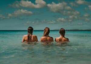 tre kvinnor i vatten som tittar ut över havet under vita moln